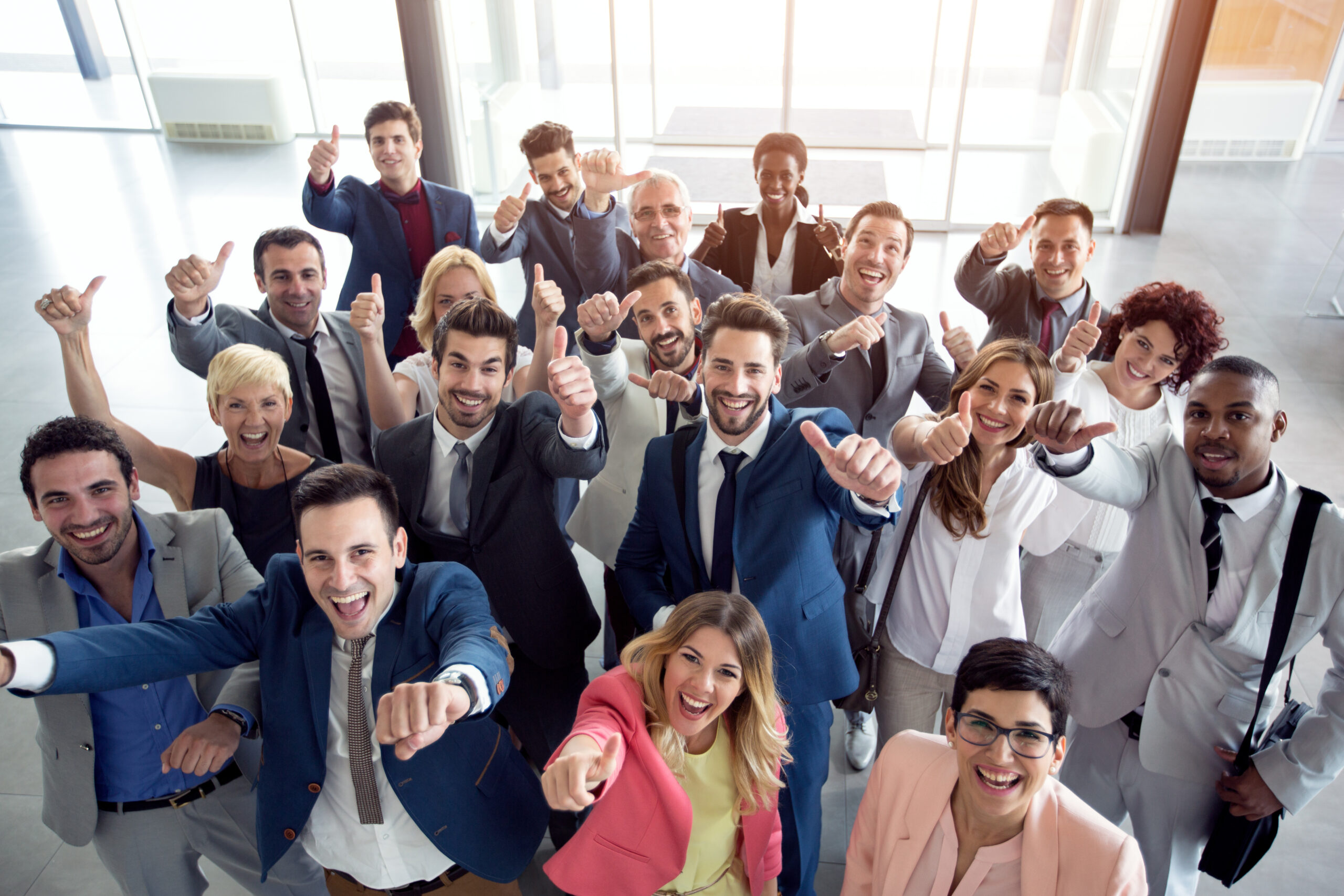 Gruppe von Neueinsteigern und Arbeitskollegen zeigt Daumen hoch und lacht.
