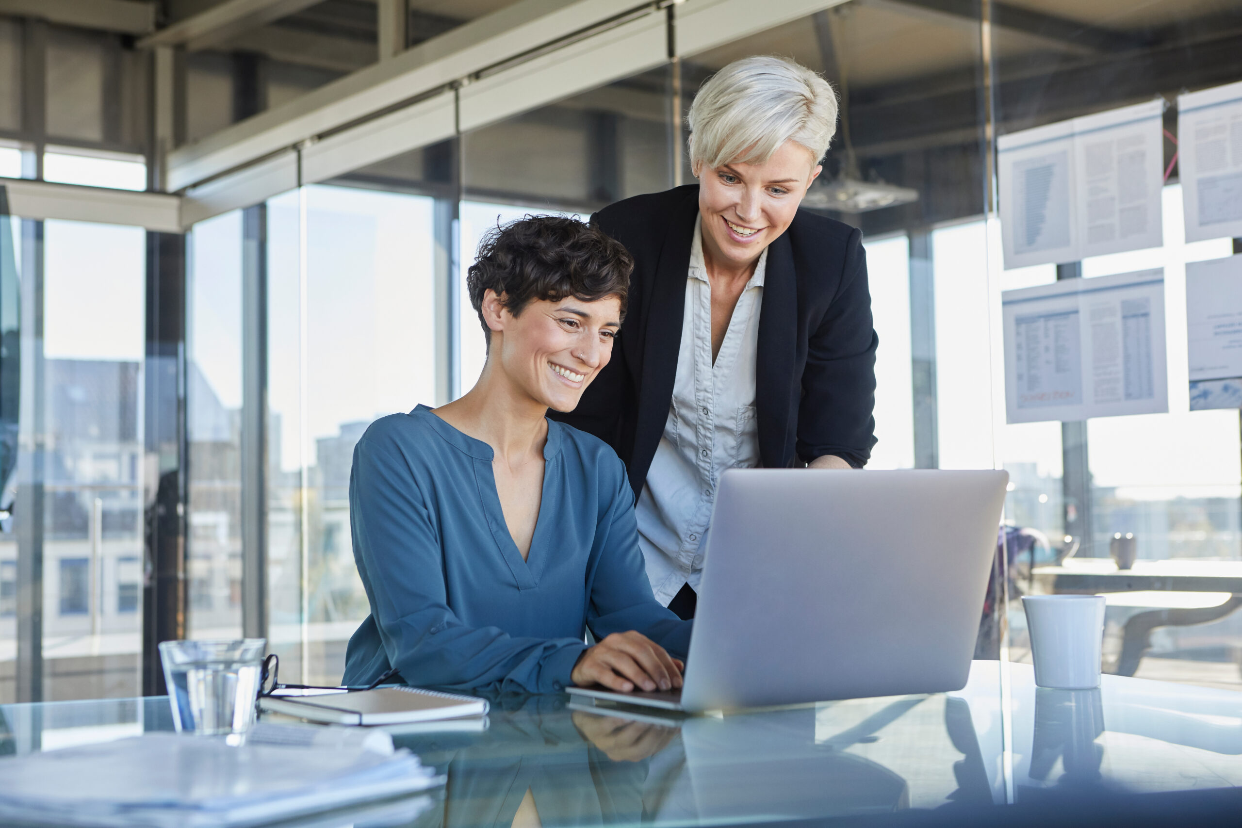 Zwei Frauen der allgemeinen Verwaltung arbeiten gemeinsam am Laptop im Büro.